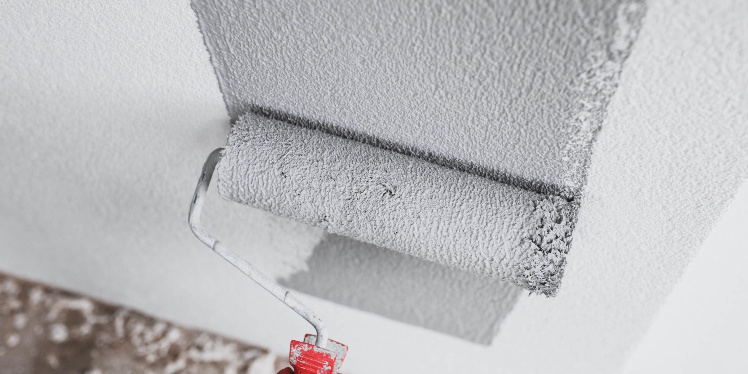 paint roller with grey paint rolling on a white wall